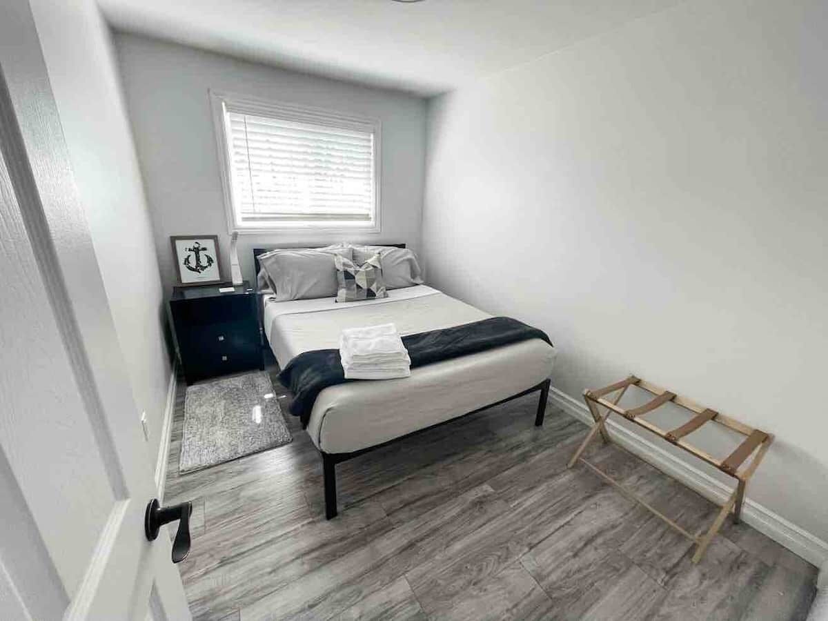 Une chambre à coucher avec un lit, une table de chevet, une fenêtre avec des stores, une échelle en bois et une porte.