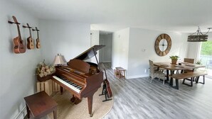Un vaste salon agrémenté d’un magnifique piano à queue, un coin repas avec une table et des chaises en bois, et une grande horloge murale.