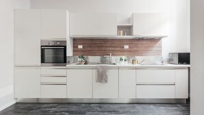 A modern kitchen with white cabinets, a built-in oven, a microwave, and a wooden backsplash. - Tristano e Isotta: Bright Three-room 6 Adults (Bologna)