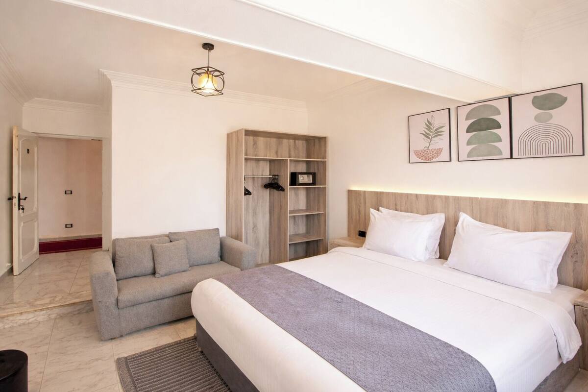 Quarto de hotel com cama, sofá, guarda-roupa e corredor.