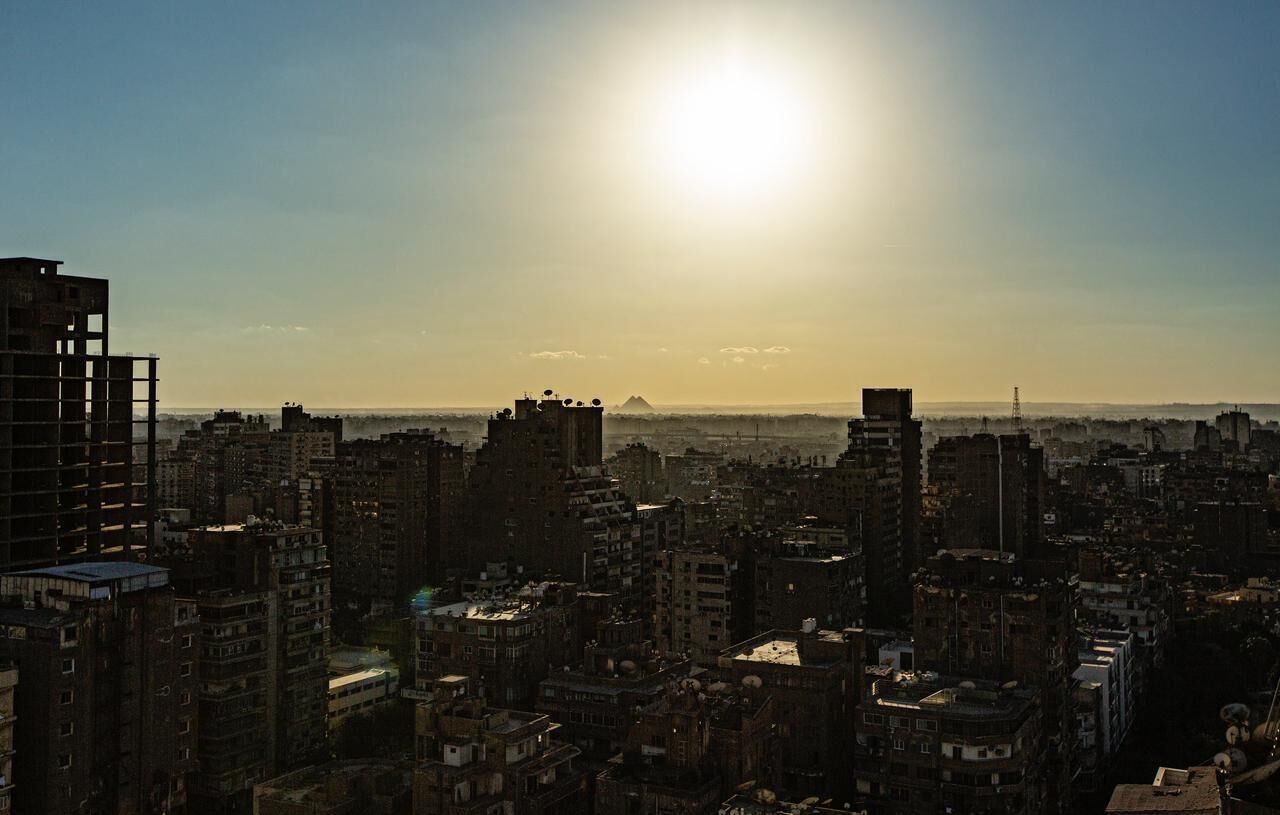 A cityscape with high-rise buildings, a clear sky, and the sun setting or rising.