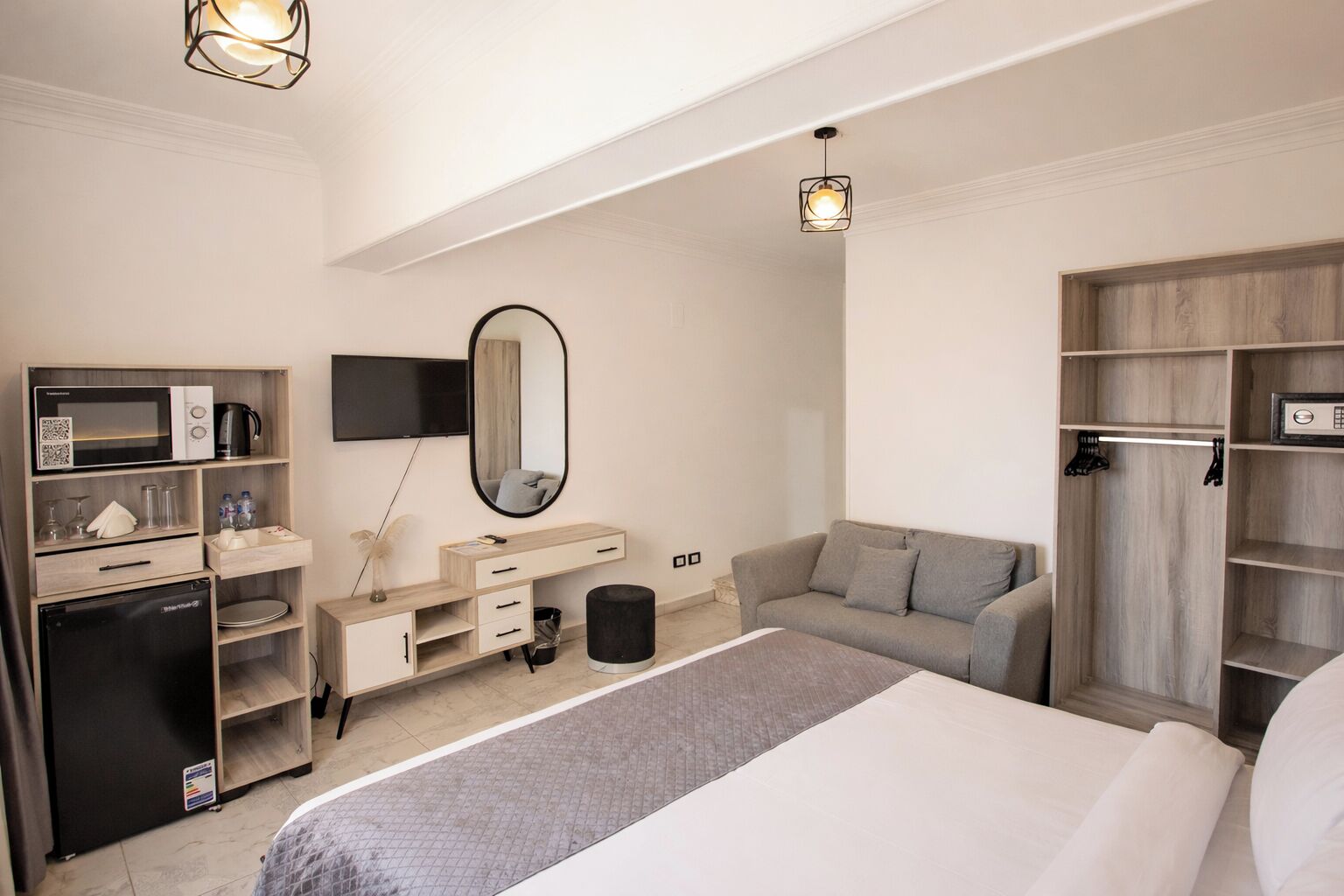 A hotel room with a bed, a desk with a microwave, a TV, a wardrobe, and a mirror.