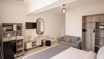 A hotel room with a bed, a desk with a microwave, a TV, a wardrobe, and a mirror.