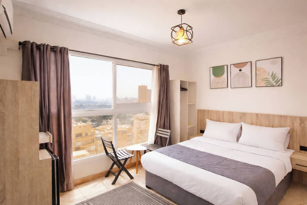 Quarto de hotel com uma janela grande, uma cama, uma escrivaninha e uma cadeira.