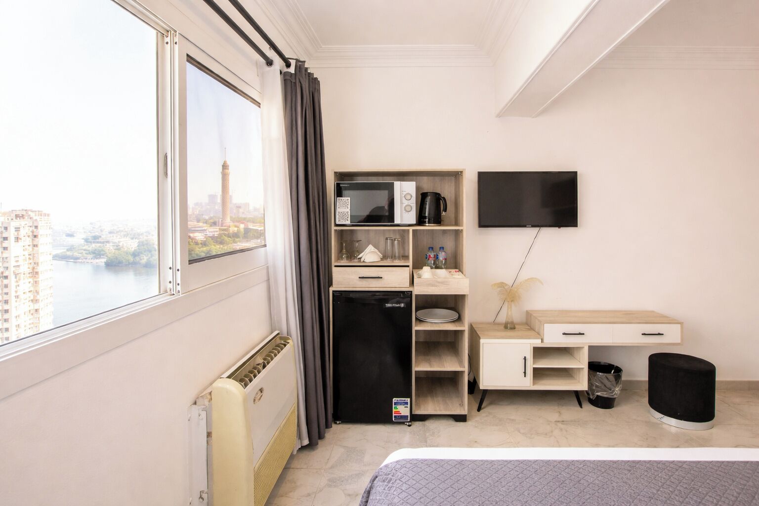A hotel room with a bed, a desk, a television, a mini-fridge, a coffee maker, and a view of a cityscape.