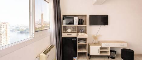 A hotel room with a bed, a desk, a television, a mini-fridge, a coffee maker, and a view of a cityscape.