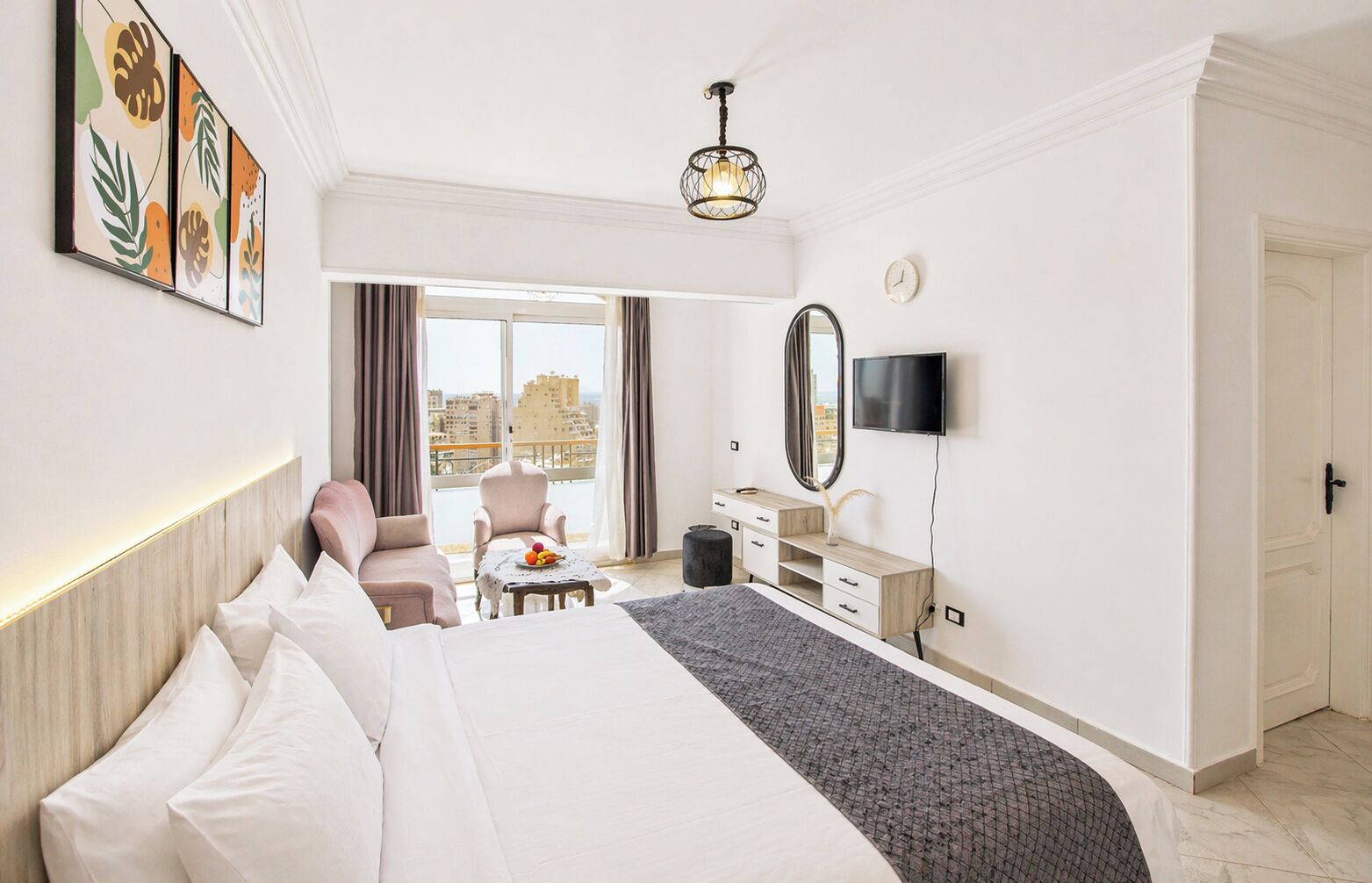 A hotel room with a bed, a desk, a chair, a TV, and a large window with a city view.