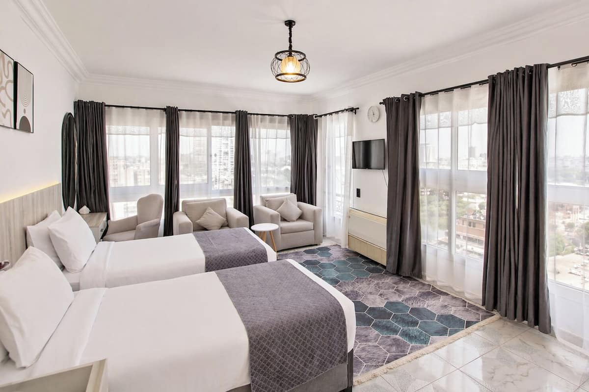 Quarto de hotel com duas camas, um sofá, televisão e vista para a cidade.