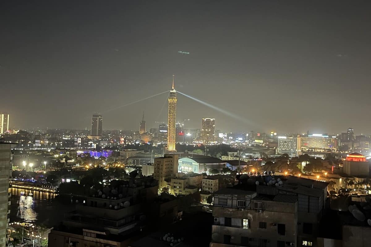 Vista noturna de uma cidade com edifícios iluminados e uma torre imponente.