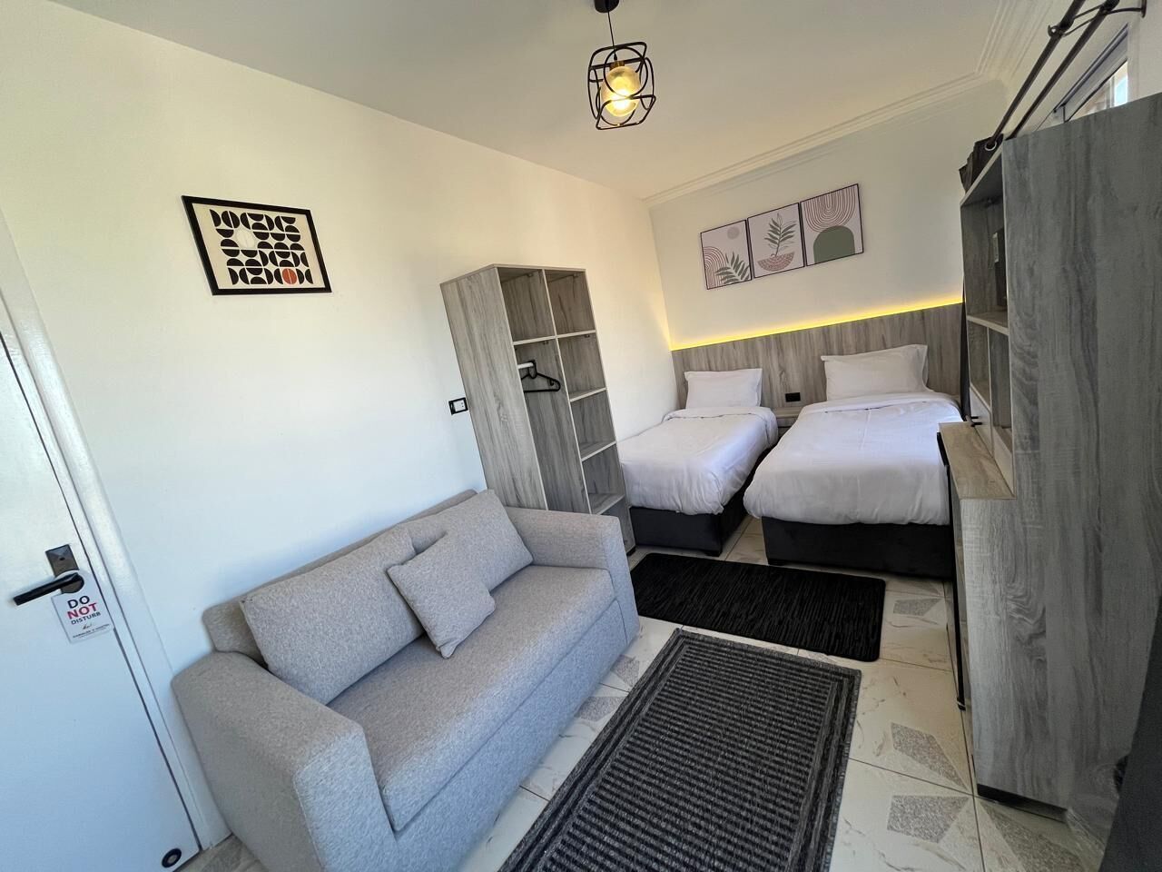 A compact room with a grey sofa, two single beds, a wardrobe, and a small cabinet.