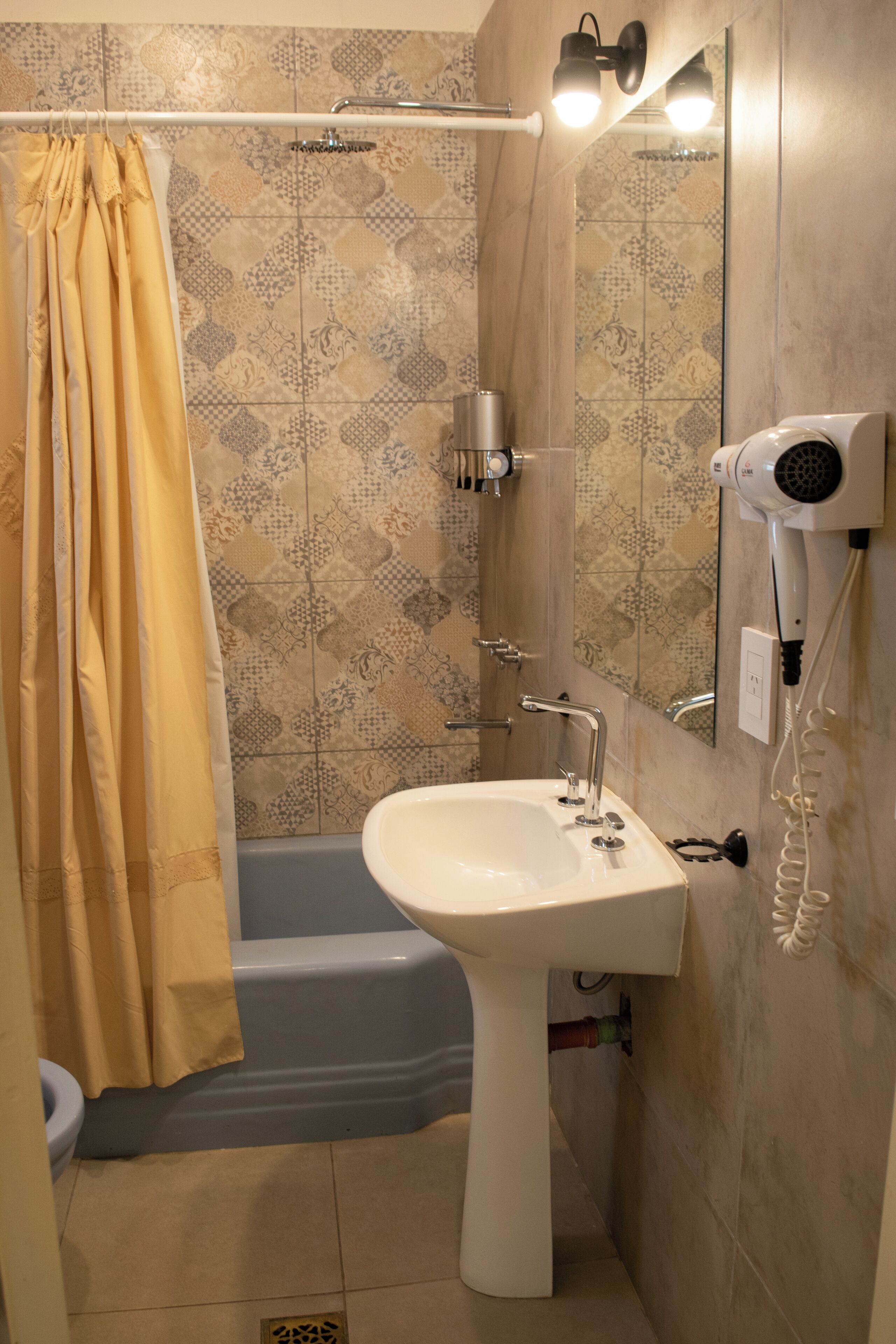 A bathroom with a bathtub, a sink, a shower curtain, and a hairdryer mounted on the wall.