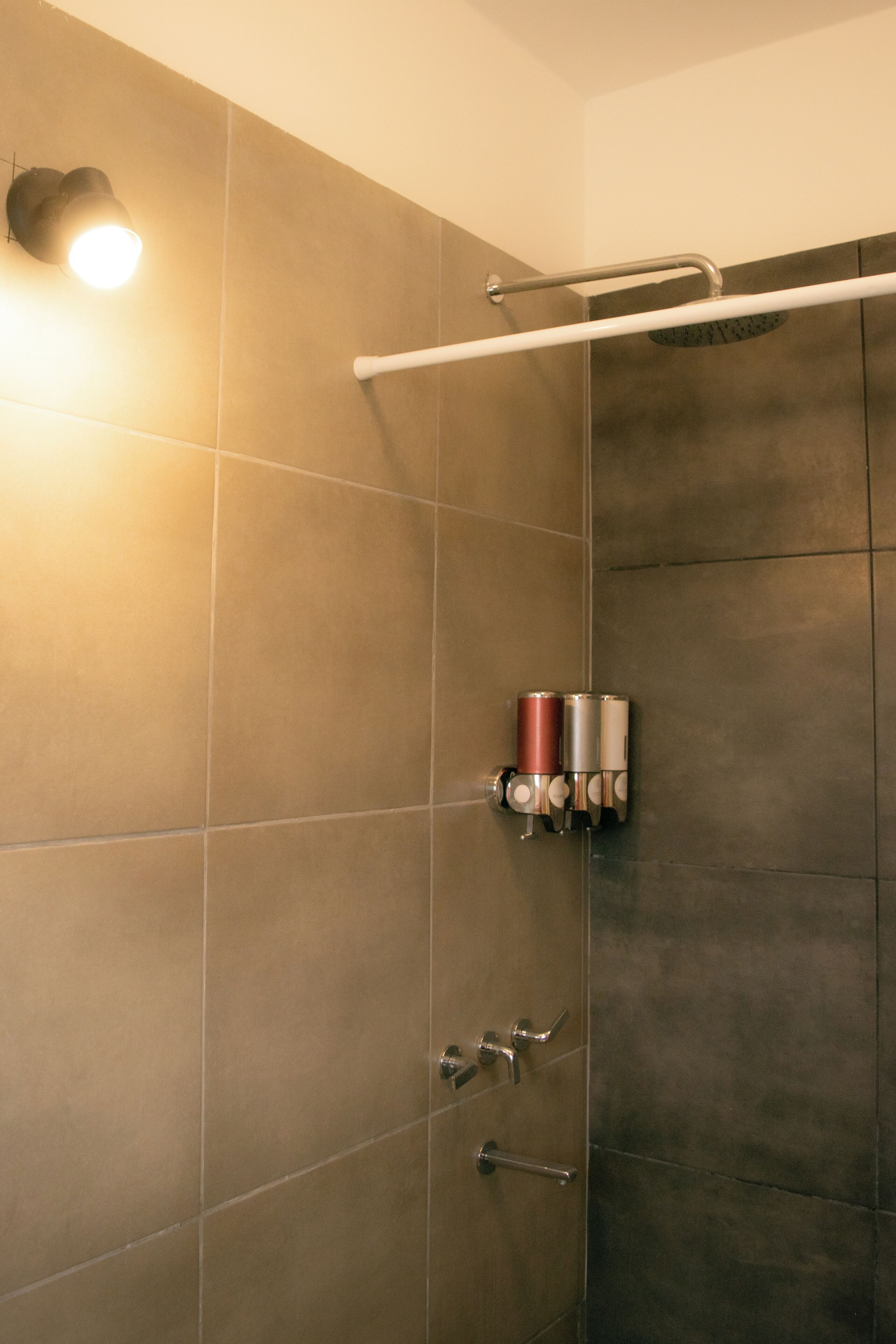 A shower area with a handrail, a wall-mounted towel dispenser, and a light fixture.