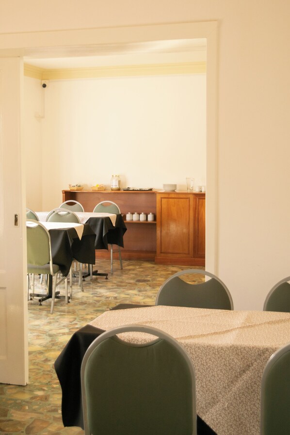 A dining area with tables and chairs, a wooden cabinet with kitchenware, and a tiled floor. - La Casona del Monumento (Salta)