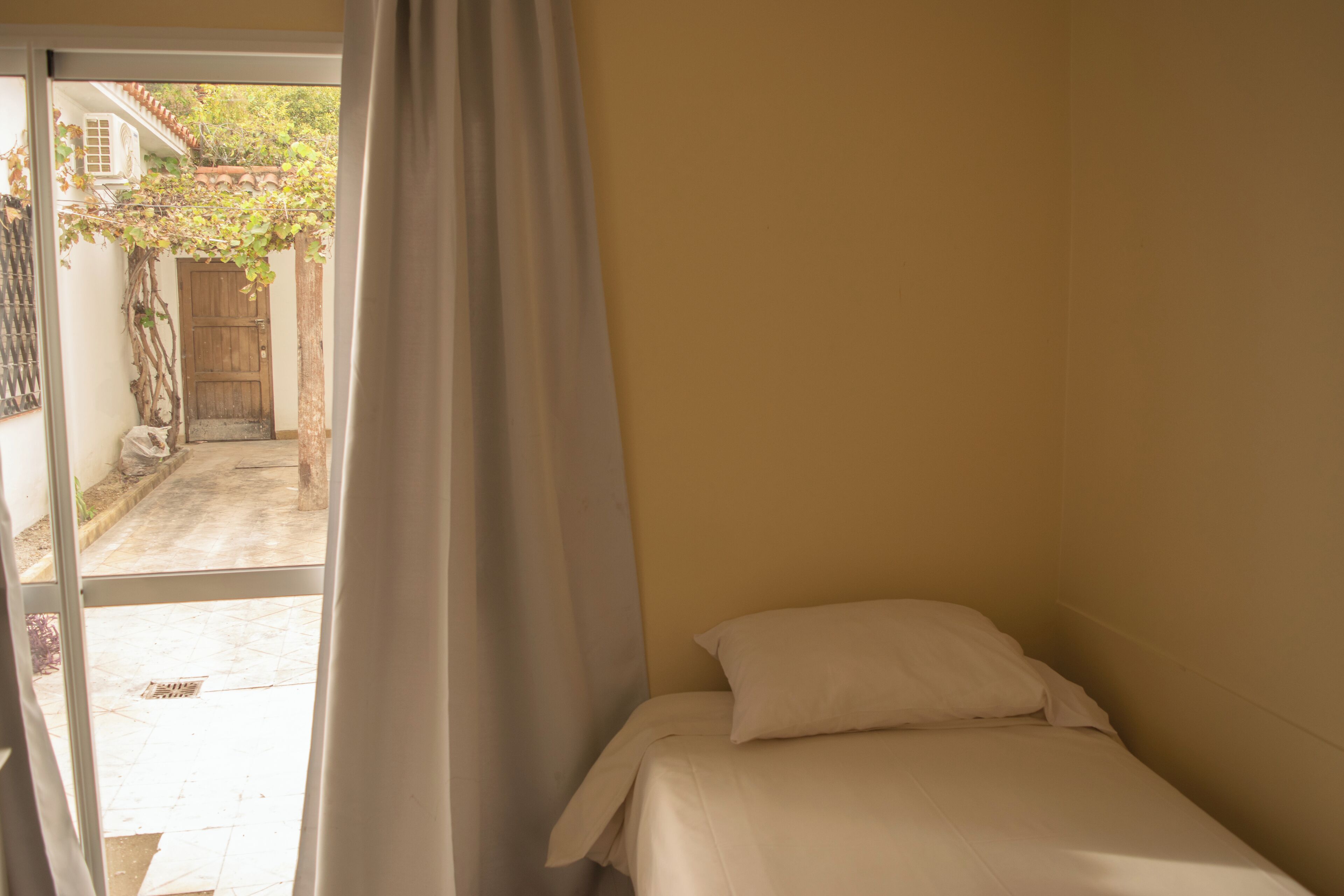 A small, single-bed room with a sliding glass door leading to a courtyard.
