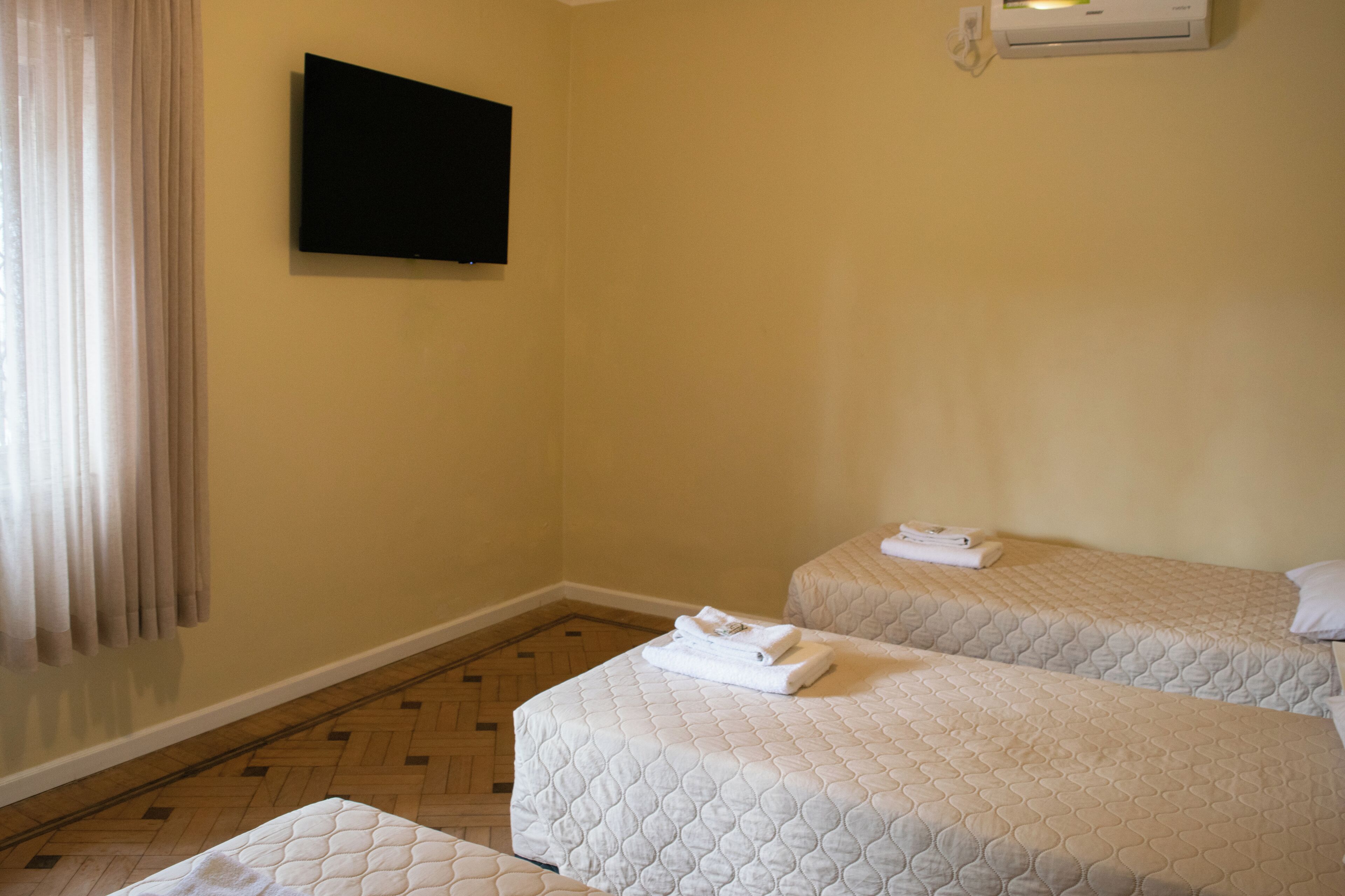 Quarto de hotel com duas camas, televisão de tela plana fixada na parede e um aparelho de ar condicionado.