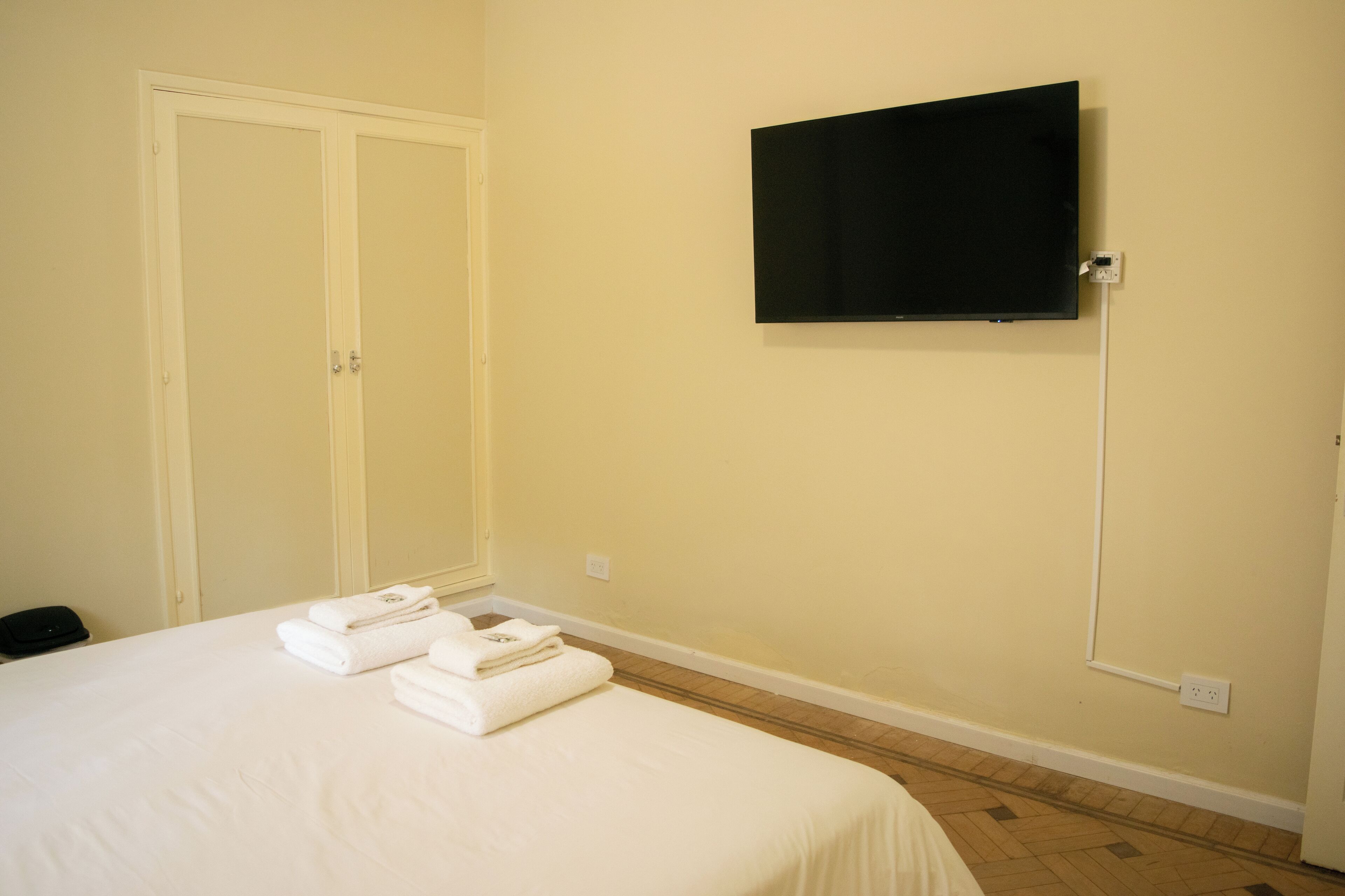 Habitación de hotel con una cama, un televisor montado en la pared y un juego de toallas ordenadas sobre la cama.