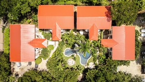 Luftaufnahme eines Resorts mit vier Gebäuden, einem Pool und üppiger Bepflanzung.