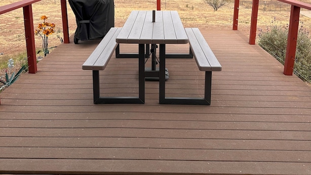 A wooden deck with a picnic table and grill, overlooking a desert landscape with distant mountains.