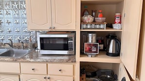 A kitchen with beige cabinets, a microwave, a sink, and a variety of kitchenware and appliances.