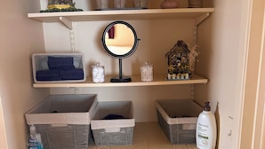 A small, organized storage area with shelves holding potted plants, a decorative birdhouse, a mirror, and storage boxes.