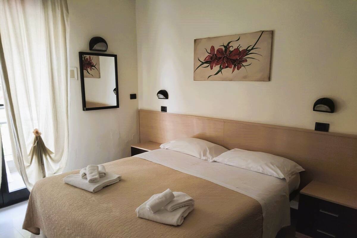 Een hotelkamer met een bed, nachtkastje, spiegel en een schilderij aan de muur.