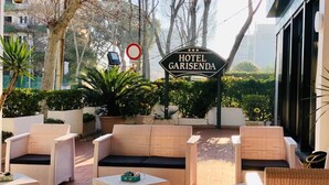 A hotel patio with wicker furniture, a sign reading "HOTEL GARISENDA," and a view of the surrounding greenery.