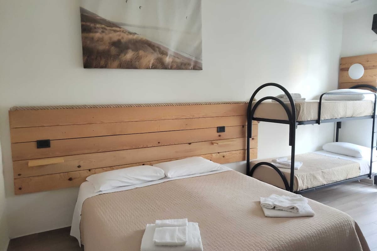 Een hotelkamer met een bed met houten hoofdeinde, een stapelbed en een schilderij aan de muur.