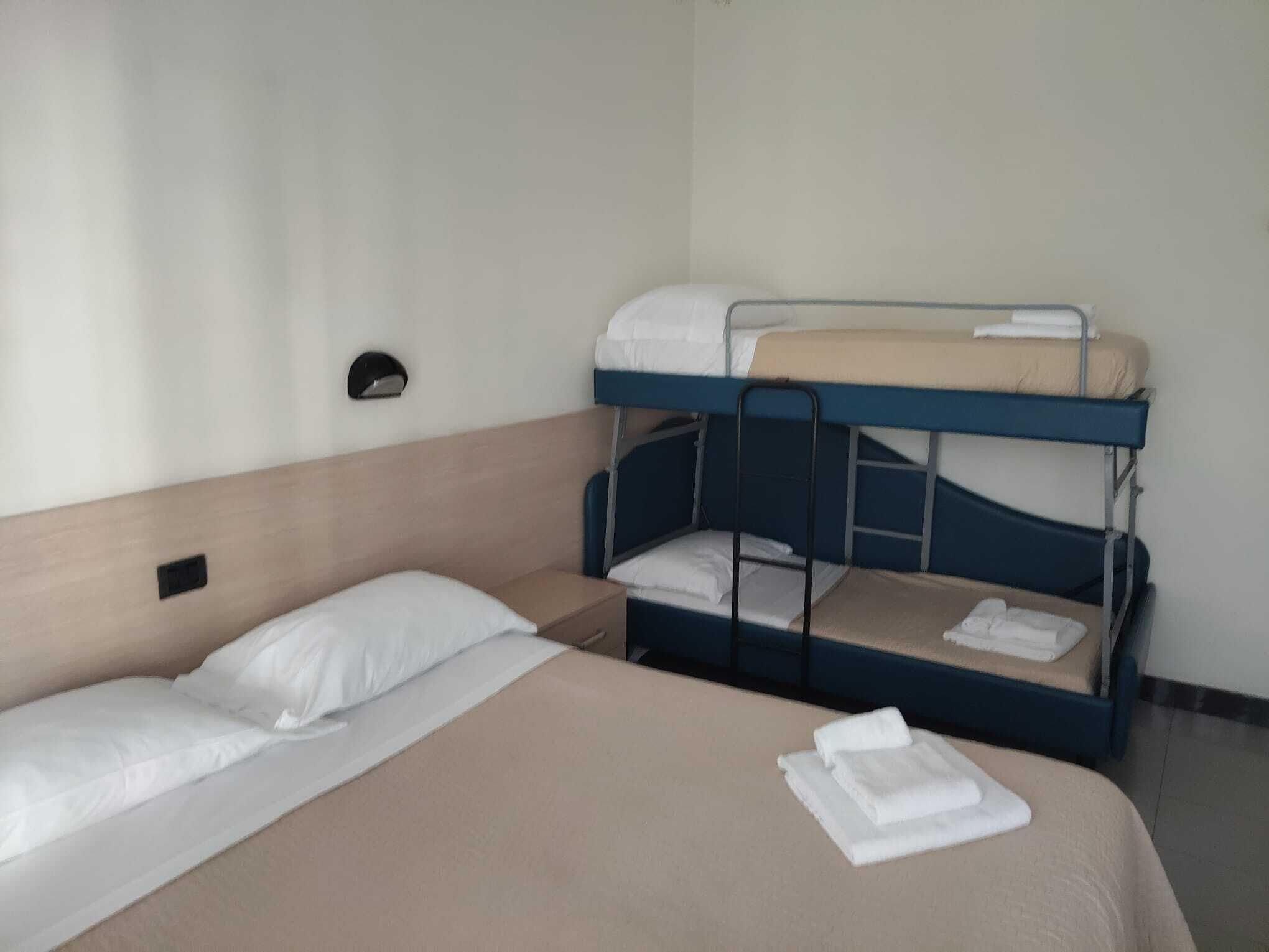 A bunk bed room with a single bed and a bunk bed. There is a wall-mounted light and a small shelf.