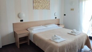 A hotel room with a large bed, two bedside tables, a wall-mounted lamp, and a window with curtains.