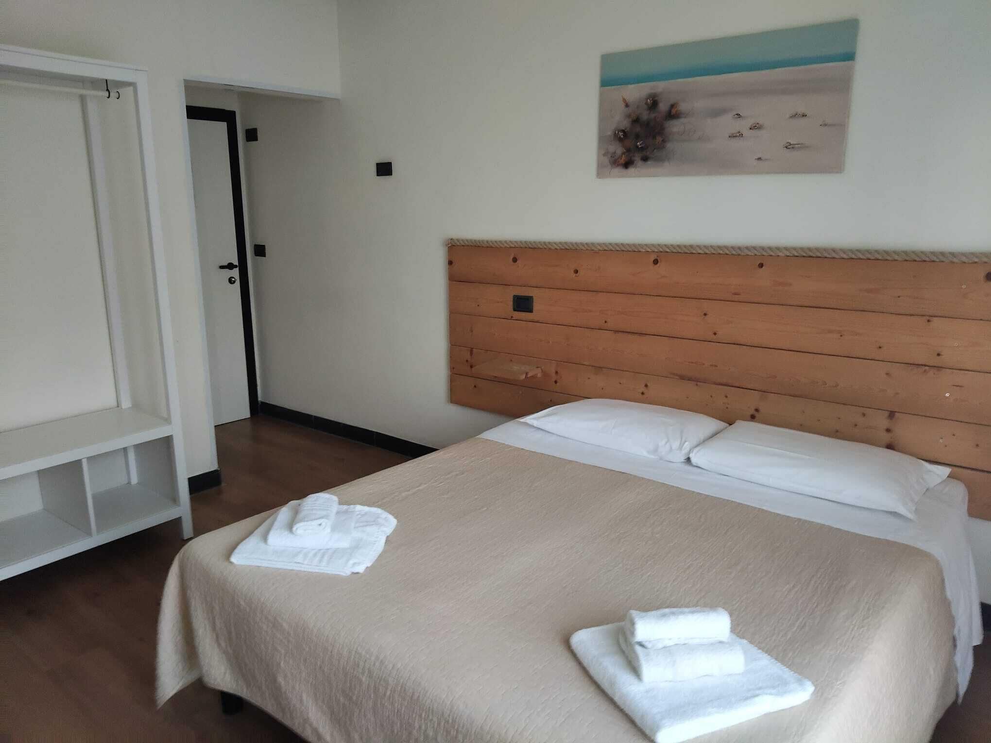 Una habitación de hotel con una cama, cabecera de madera, un cuadro en la pared y un armario blanco.