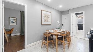 Un comedor con una mesa y sillas de madera, una obra de arte enmarcada en la pared, y una puerta que da a otra habitación.