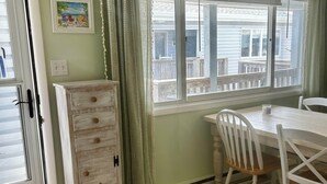 Una habitación con un aparador de madera, una mesa de comedor con sillas, un tapete estampado y una ventana con persianas.