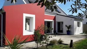 A modern house with a red and white exterior, a paved driveway, and a small garden with plants and a tree. - Large, comfortable Grand-Cosquet Locmaria house on 800m2 wooded grounds (Locmaria)
