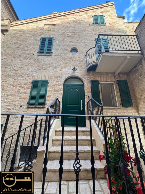 A stone building with a green door, a balcony, and a staircase leading to the entrance.