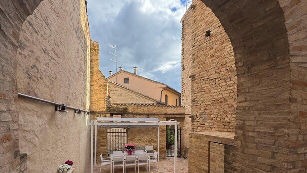 An arched courtyard with a brick floor, a pergola, and a table with chairs. - La Dimora del Borgo (Montecassiano)