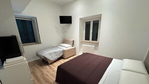A bedroom with a single bed, a smaller bed, a TV mounted on the wall, and a window with shutters. - La Dimora del Borgo (Montecassiano)