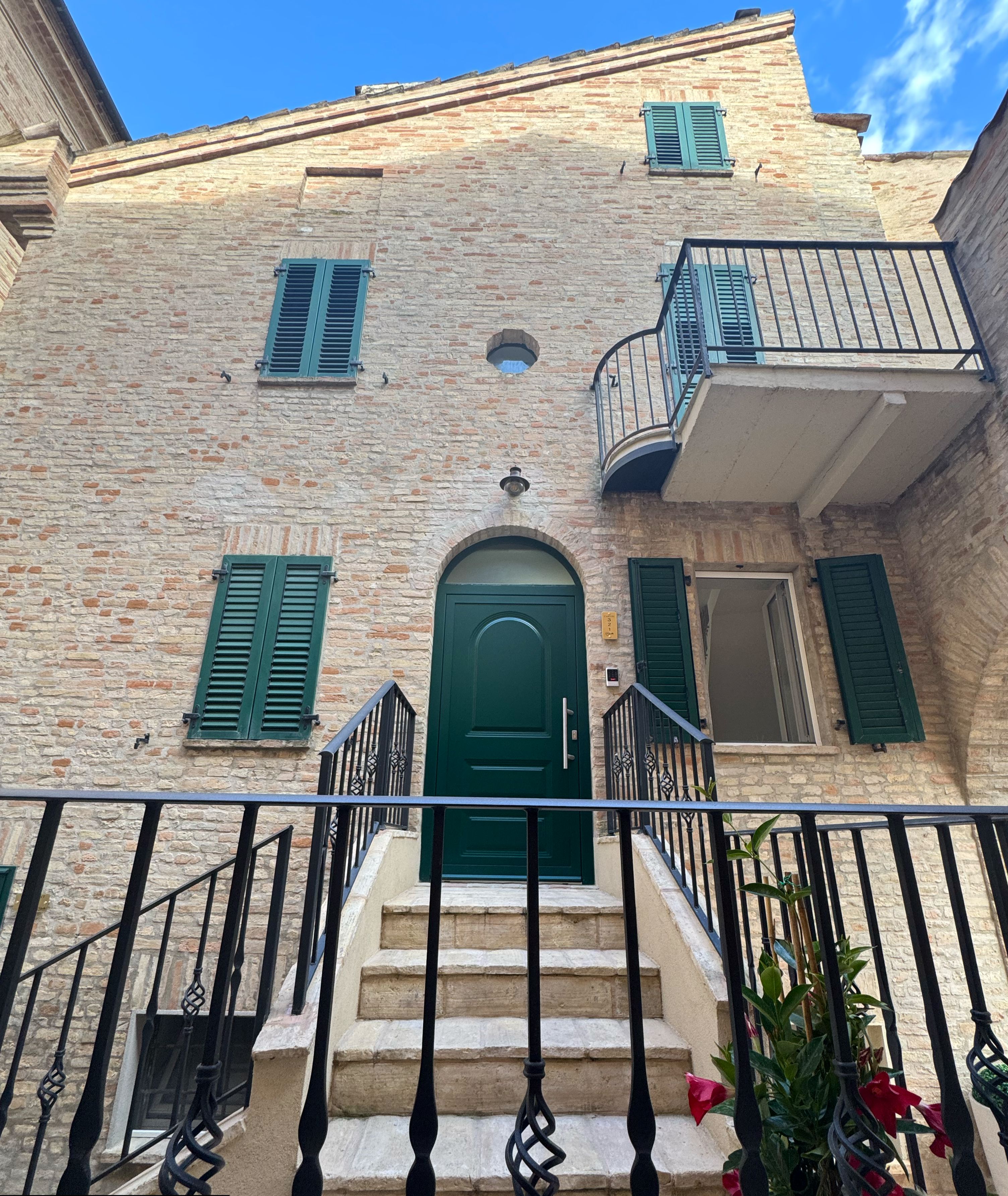 A stone building with a green door, a balcony, and a staircase leading to the entrance.