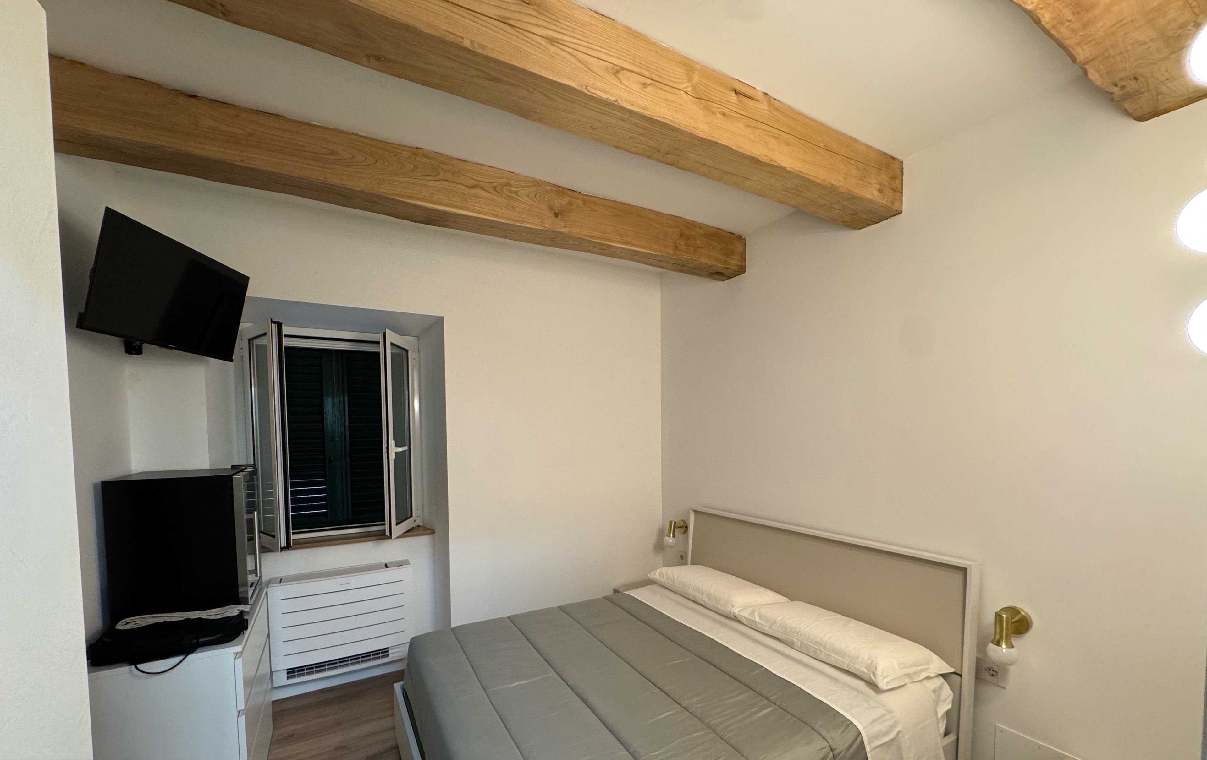 A bedroom with a bed, a TV, a window, and a heater.