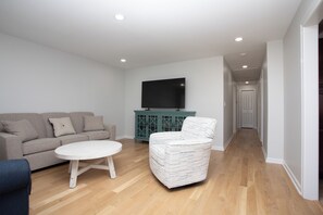 A modern living room with a sofa, a coffee table, and a patterned armchair. A flat-screen TV is mounted on the wall, and a teal cabinet is visible in the background. - Charming newly renovated 3-bedroom house two blocks from sandy beach (Keansburg)