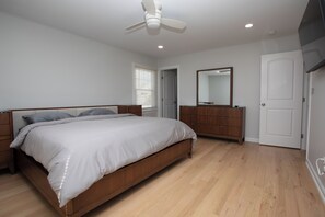 A bedroom with a bed, wooden dresser, mirror, ceiling fan, and a door. - Charming newly renovated 3-bedroom house two blocks from sandy beach (Keansburg)