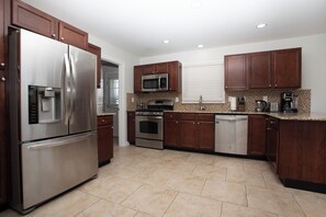 A modern kitchen with stainless steel appliances, wooden cabinets, and a tiled floor. - Charming newly renovated 3-bedroom house two blocks from sandy beach (Keansburg)
