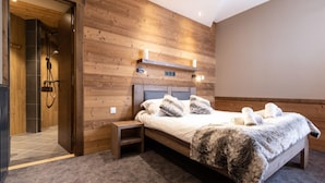 Une chambre avec un mur en bois, un lit recouvert d’une couverture moelleuse, une table de chevet et un espace douche.