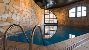 Une piscine intérieure aux murs en pierre, avec vue sur l’extérieur à travers des fenêtres en arc de cercle.