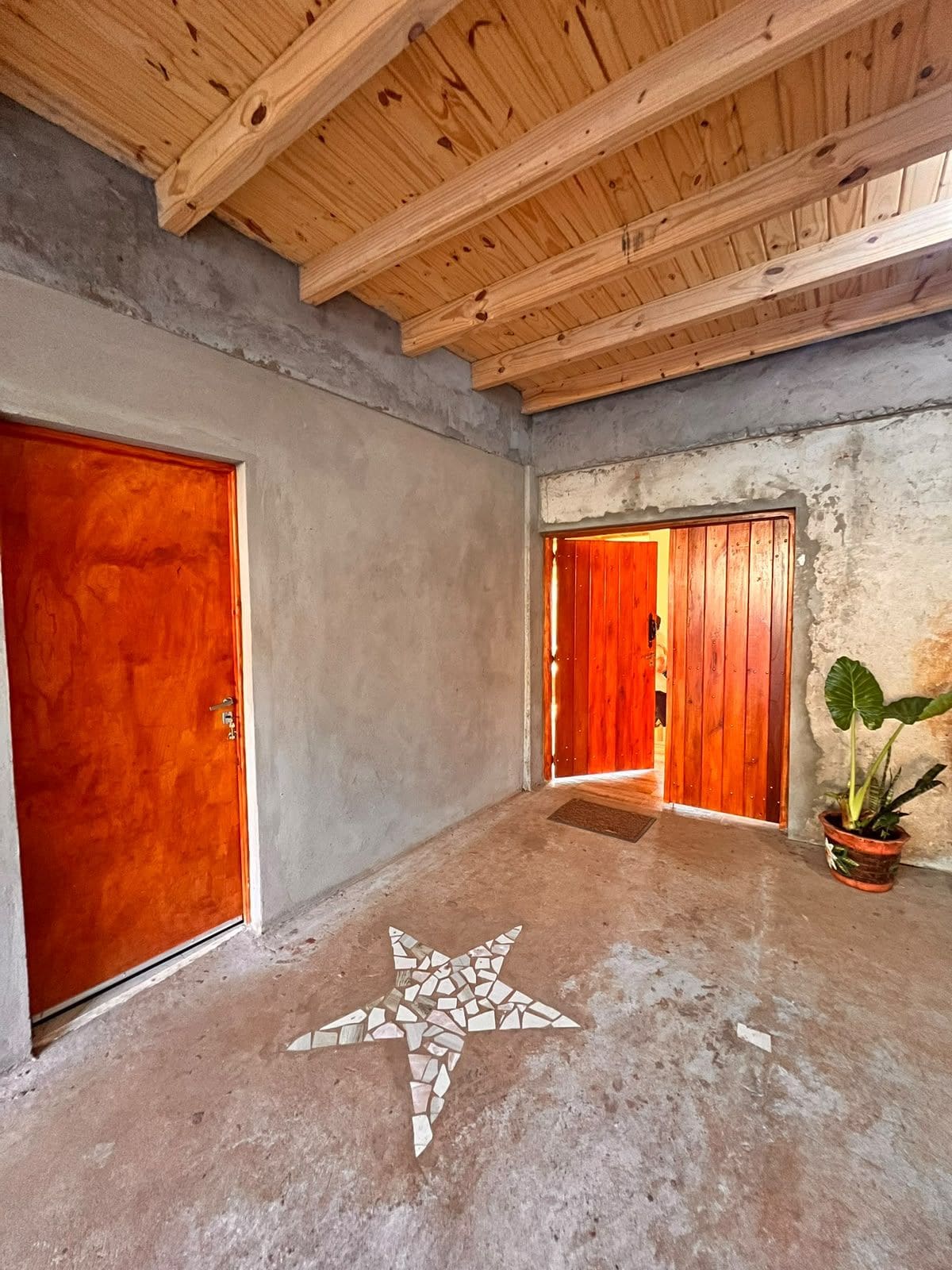 Quarto com piso de concreto, vigas de madeira no teto e duas portas de madeira.