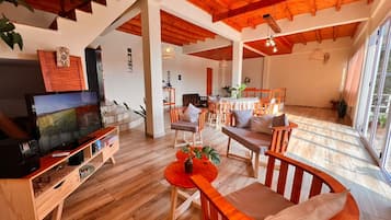 Uma sala de estar ampla com teto de madeira, uma televisão e um espaço de refeições com mobiliário de madeira.