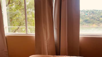 A room with a bed, a window with curtains, and a view of a river and greenery.
