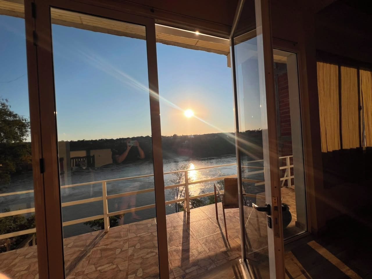 Quarto com porta de vidro que dá para uma varanda com vista para um rio e uma ponte.