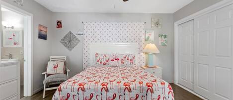Un dormitorio con cama, mesita de noche, silla, ventilador de techo y puerta.