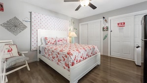 A bedroom with a bed, a ceiling fan, a nightstand, a chair, and a door with a 'No Smoking' sign.