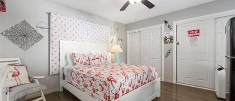 Un dormitorio con cama, ventilador de techo, mesita de noche, una silla y una puerta con un letrero de 'No Fumar'.